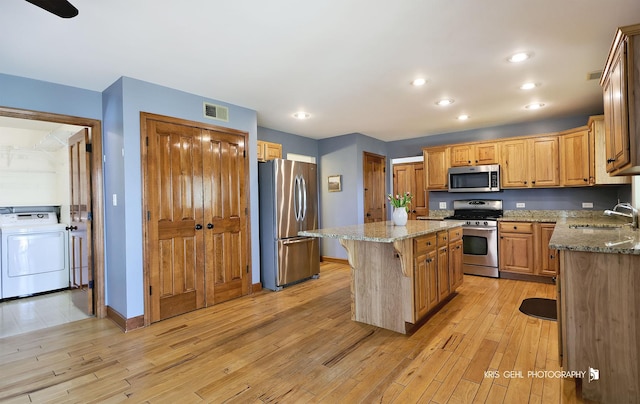 kitchen with appliances with stainless steel finishes, a sink, a kitchen island, light wood-style flooring, and recessed lighting