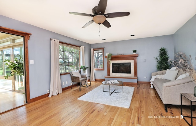 living room with light wood-style flooring, a ceiling fan, a glass covered fireplace, and baseboards