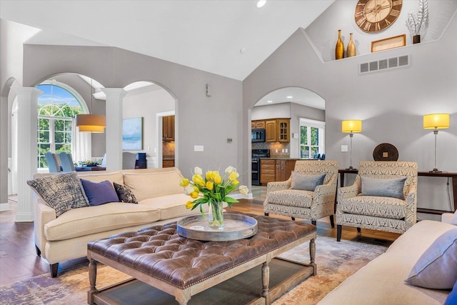 living area featuring arched walkways, plenty of natural light, light wood-type flooring, and high vaulted ceiling