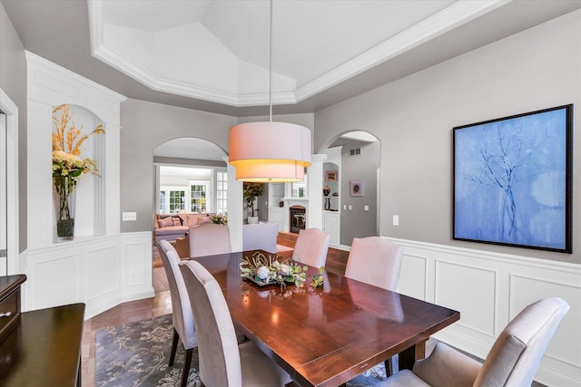dining area with arched walkways, a tray ceiling, visible vents, and a decorative wall