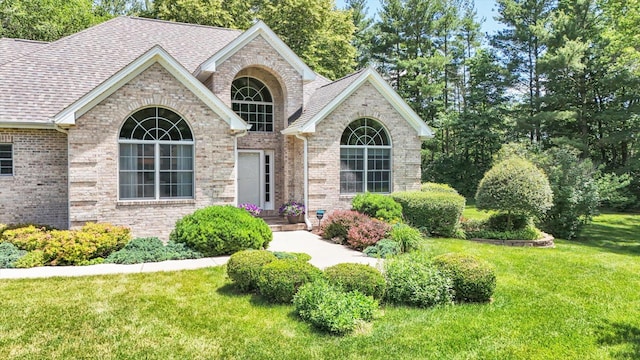 view of front of home featuring brick siding, roof with shingles, and a front yard