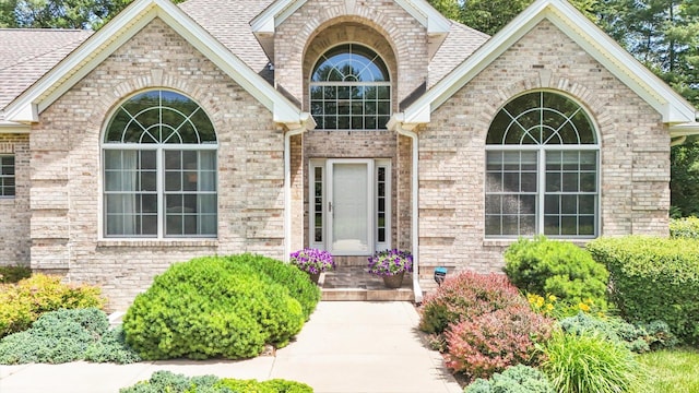 doorway to property featuring brick siding and roof with shingles