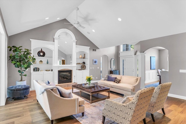 living room featuring built in features, ceiling fan, high vaulted ceiling, arched walkways, and light wood finished floors
