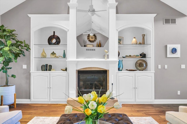 living room with ceiling fan, visible vents, built in shelves, wood finished floors, and a glass covered fireplace