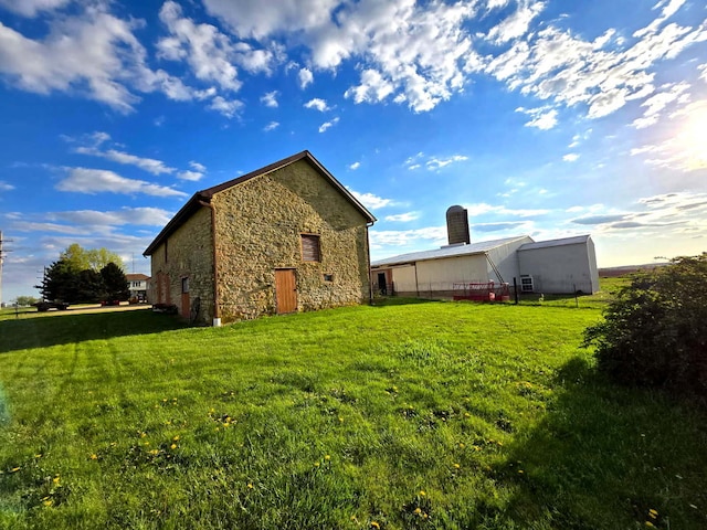 8554 S Daysville Rd, Franklin Grove, IL 61031 - view of side of property featuring stone siding, a yard, a pole building, and an outdoor structure