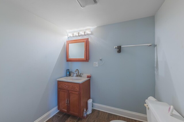 half bathroom with toilet, baseboards, wood finished floors, and vanity