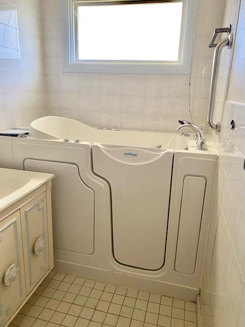 bathroom featuring tile patterned floors, tile walls, a whirlpool tub, and vanity