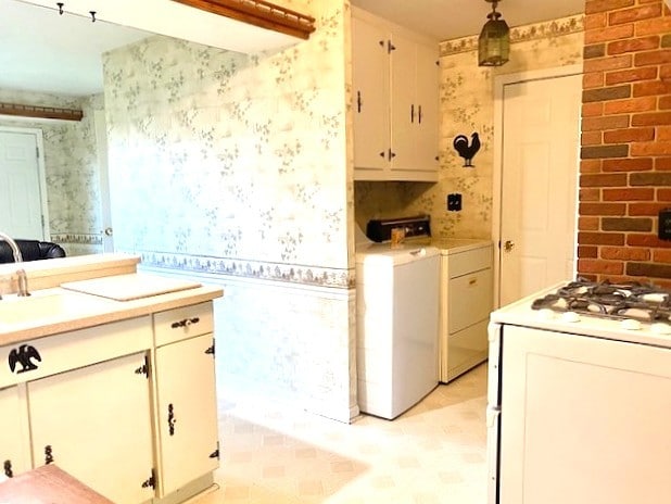 kitchen with white range with gas cooktop, washing machine and clothes dryer, light countertops, white cabinets, and wallpapered walls