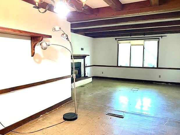 spare room with baseboards, beam ceiling, and a fireplace with raised hearth
