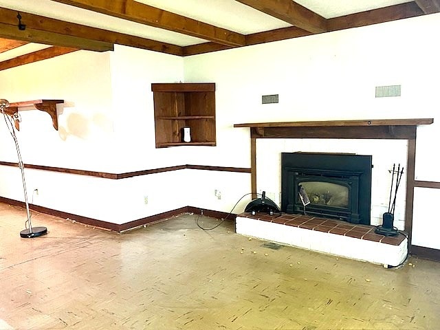 unfurnished living room with beamed ceiling, baseboards, and visible vents