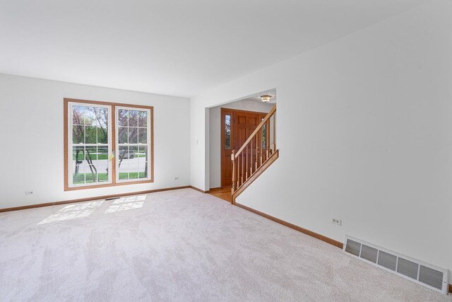carpeted spare room with visible vents, baseboards, and stairs