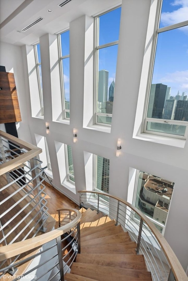 staircase featuring a towering ceiling, plenty of natural light, wood finished floors, and visible vents