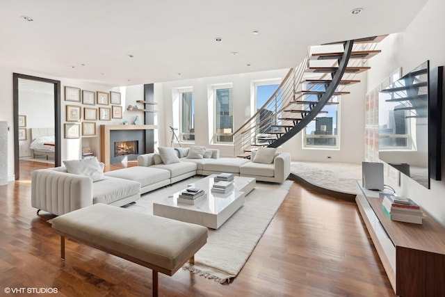 living area featuring stairs, recessed lighting, a lit fireplace, and wood finished floors