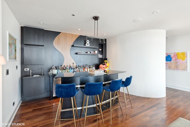 bar with dark wood-style flooring, hanging light fixtures, a sink, recessed lighting, and bar area