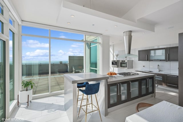 kitchen with a kitchen breakfast bar, island exhaust hood, expansive windows, a sink, and stainless steel gas stovetop