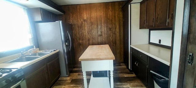 kitchen with stainless steel fridge, gas range oven, dark brown cabinetry, dark wood-type flooring, and wooden walls
