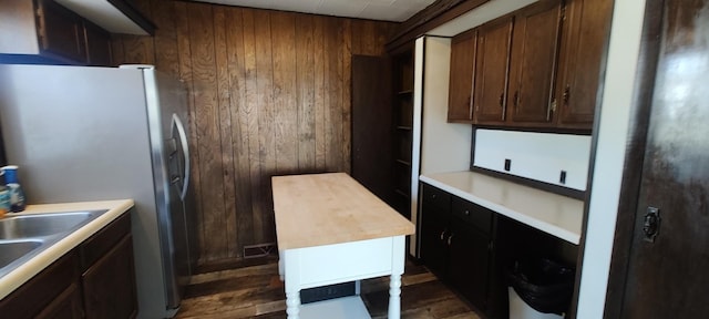 kitchen with dark wood finished floors, a sink, wooden walls, stainless steel refrigerator with ice dispenser, and light countertops