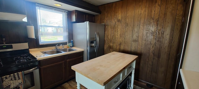 kitchen with a sink, wood walls, butcher block counters, under cabinet range hood, and appliances with stainless steel finishes