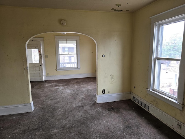 carpeted empty room featuring arched walkways, baseboards, and visible vents