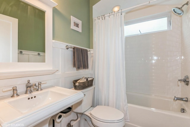 bathroom featuring toilet, shower / tub combo with curtain, a wainscoted wall, and a sink