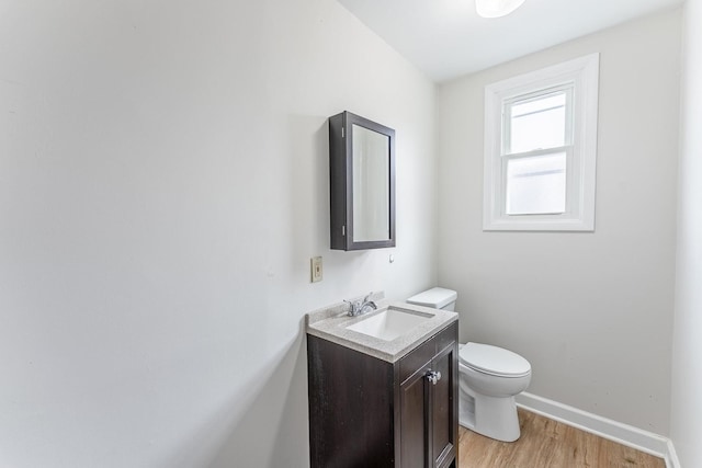 half bathroom featuring vanity, toilet, baseboards, and wood finished floors