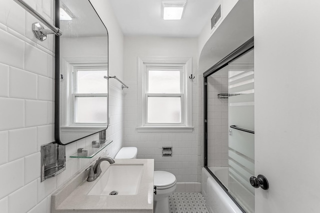full bath with tile walls, toilet, visible vents, and plenty of natural light