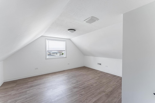 additional living space featuring baseboards, visible vents, wood finished floors, and lofted ceiling