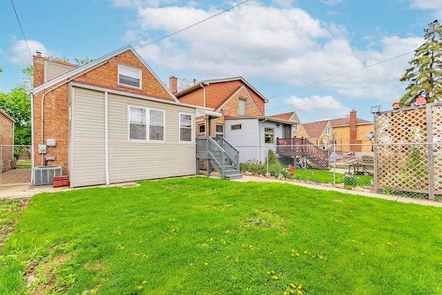 back of property with a chimney, a yard, brick siding, fence, and central AC unit