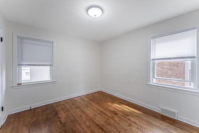unfurnished room with a wealth of natural light, baseboards, visible vents, and wood finished floors