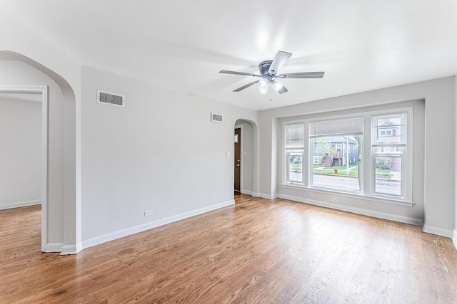 unfurnished room with visible vents, wood finished floors, a ceiling fan, and arched walkways