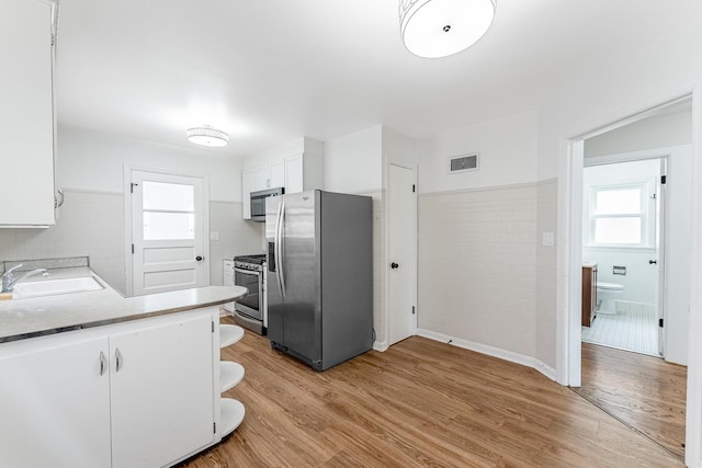 kitchen with light wood finished floors, visible vents, a sink, white cabinetry, and stainless steel appliances