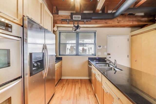 kitchen featuring appliances with stainless steel finishes, a sink, light wood-style floors, beamed ceiling, and baseboards