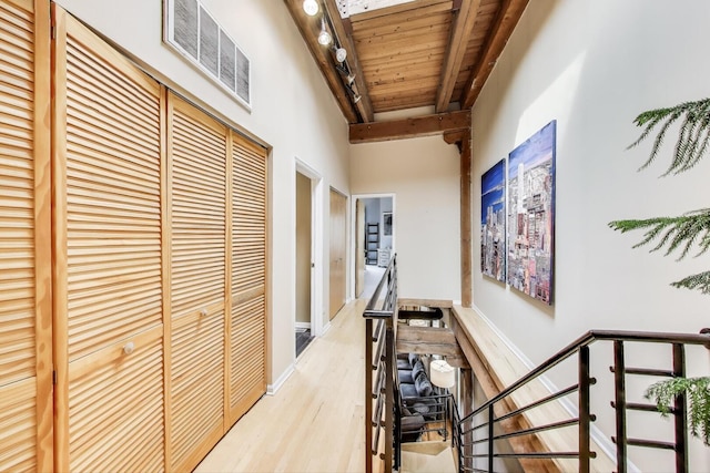hallway featuring an upstairs landing, wood finished floors, beam ceiling, and wooden ceiling