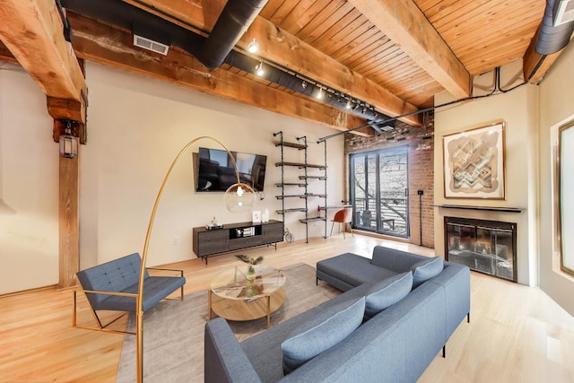living room featuring wooden ceiling, wood finished floors, beamed ceiling, and a glass covered fireplace