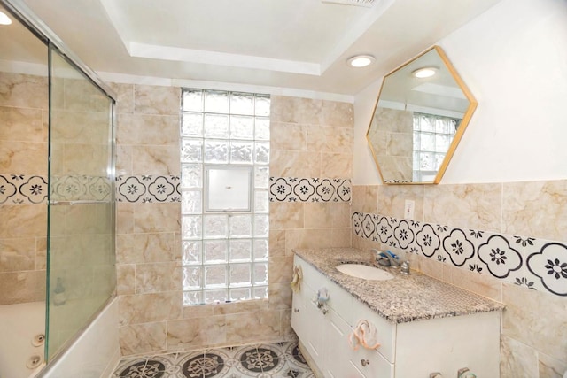 full bath with shower / bath combination with glass door, a raised ceiling, vanity, tile patterned floors, and tile walls