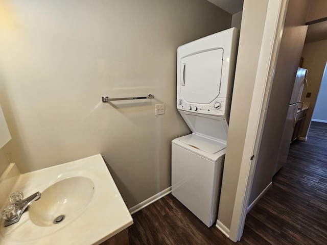 laundry room featuring laundry area, baseboards, stacked washing maching and dryer, dark wood-type flooring, and a sink