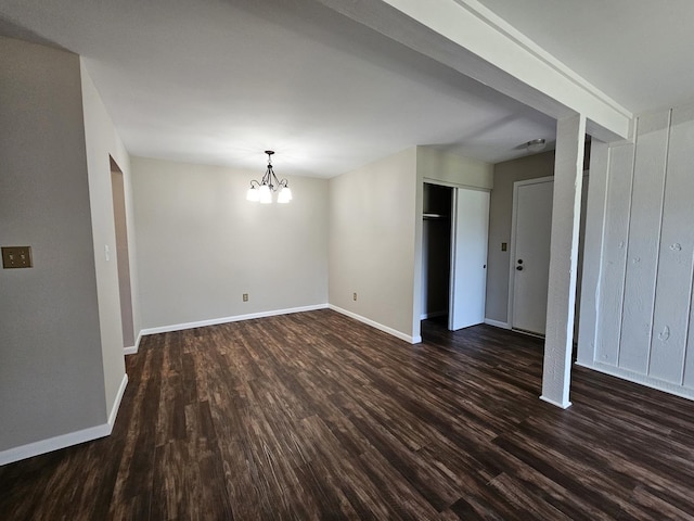 empty room with baseboards, a chandelier, and dark wood-type flooring