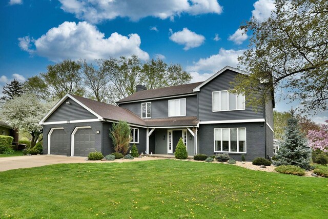 traditional home featuring an attached garage, driveway, a front yard, and a chimney