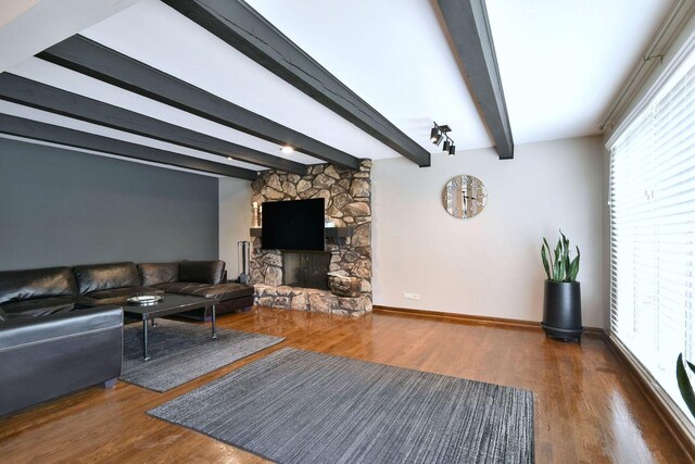 living area with beamed ceiling, plenty of natural light, wood finished floors, and a stone fireplace