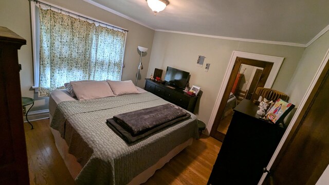 bedroom with ornamental molding and wood finished floors