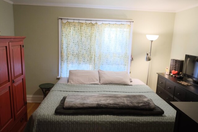 bedroom featuring baseboards, ornamental molding, and wood finished floors