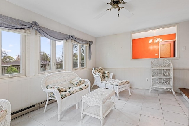 living area with tile patterned floors, a baseboard heating unit, wainscoting, and ceiling fan with notable chandelier