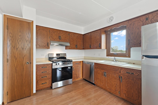 kitchen featuring under cabinet range hood, appliances with stainless steel finishes, brown cabinetry, and a sink