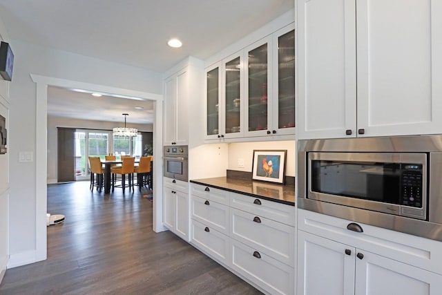 kitchen with appliances with stainless steel finishes, dark countertops, white cabinetry, glass insert cabinets, and dark wood-style floors