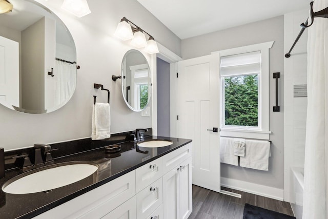 bathroom featuring double vanity, shower / bathtub combination with curtain, and wood finished floors
