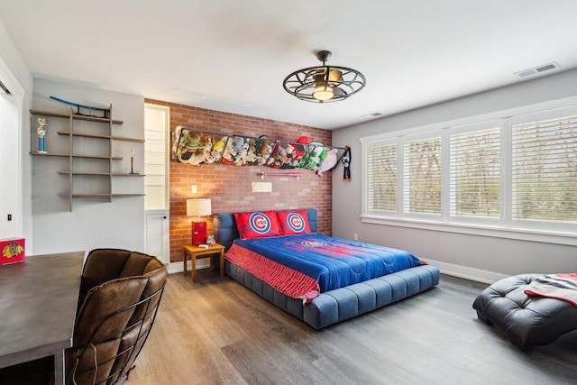 bedroom featuring wood finished floors and brick wall