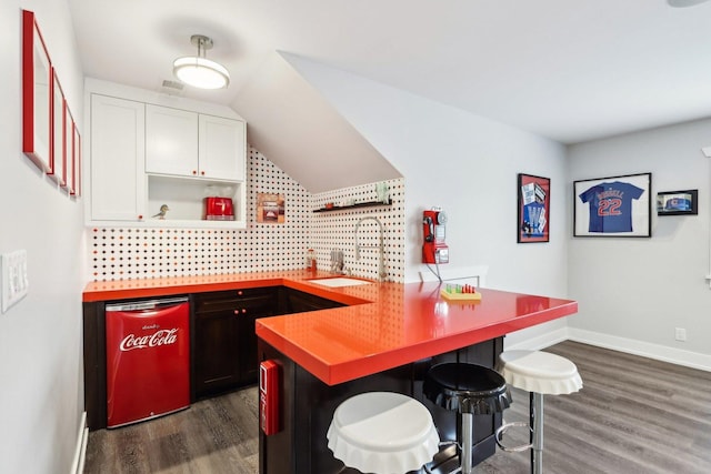 kitchen featuring dishwashing machine, a peninsula, dark wood-style floors, open shelves, and a breakfast bar