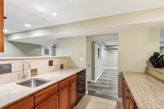 kitchen with wine cooler, a sink, light stone counters, backsplash, and brown cabinetry