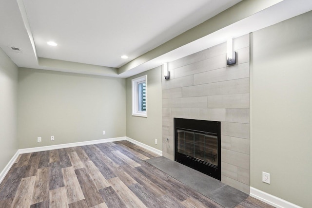 unfurnished living room featuring wood finished floors, a tile fireplace, baseboards, recessed lighting, and a raised ceiling