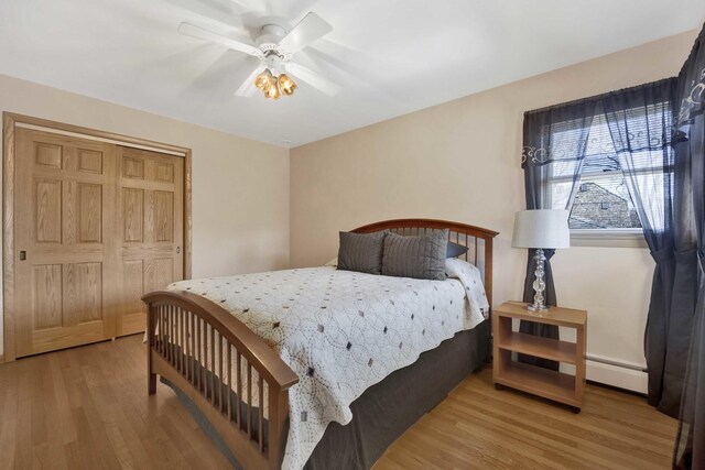 bedroom featuring ceiling fan, a baseboard heating unit, wood finished floors, and a closet